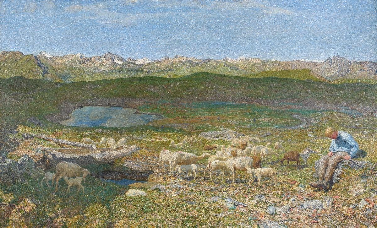 Segantini, Alpine Pasture (Pascoli alpini): a sunlit high-mountain pasture where a shepherd boy in a pale blue shirt rests on a rock at right while a small flock of sheep and lambs with a goat graze around a little blue tarn, a long chain of hazy snow-flecked peaks under a bright blue sky.